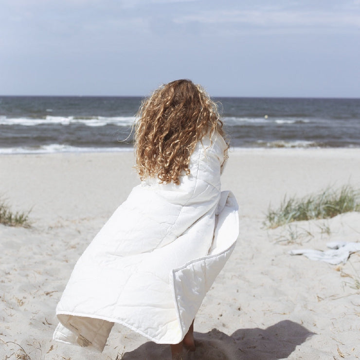 Mädchen am Meer, eingewickelt in Bio-Kinderbettdecke